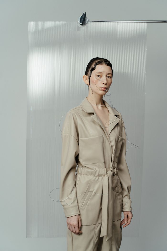Model in a sand-coloured jumpsuit behind ribbed glass, by cottonbro studio on Pexels