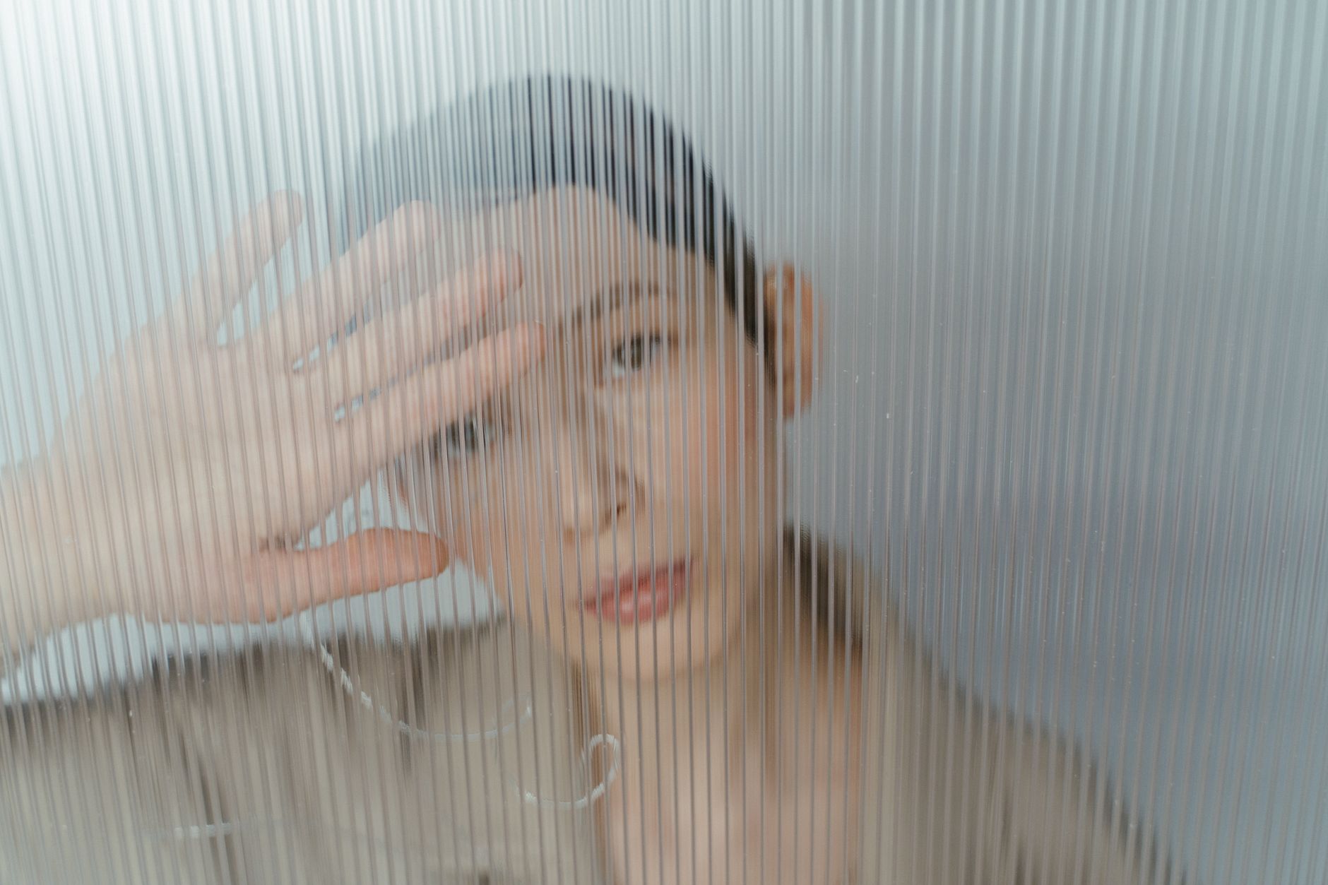 Close-up conceptual image of an adult woman partially obscured by textured glass, conveying mystery.