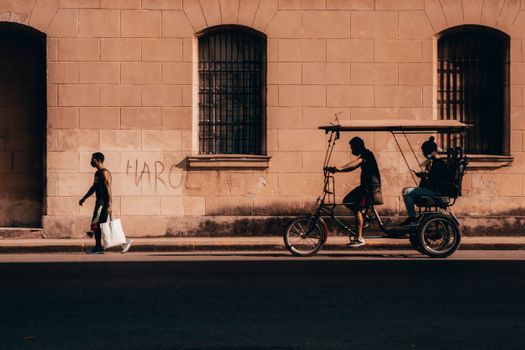 Street scene in La Habana with people walking and riding tricycles, capturing urban life.