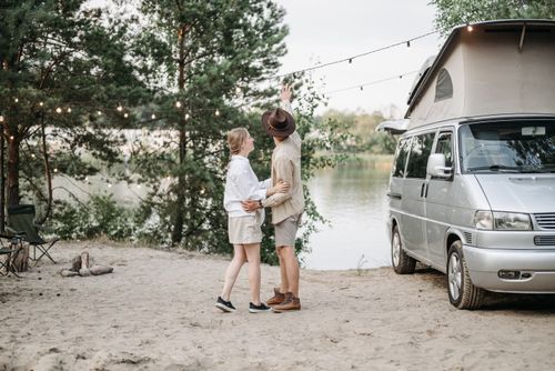 Free Couple embracing under string lights by a camper van next to a serene river. Stock Photo