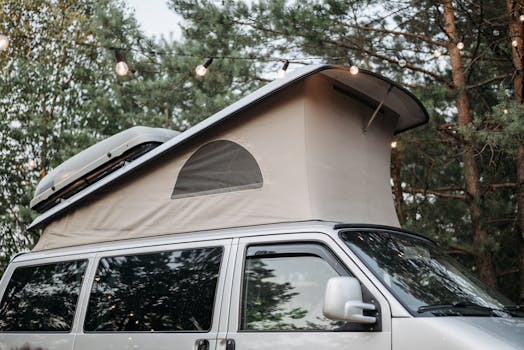 Pop-up campervan roof surrounded by string lights in a tranquil forest ambiance.