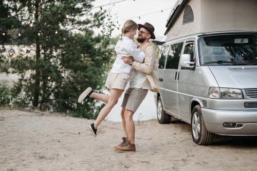 Free Happy couple embracing near a camper van, enjoying a summer adventure outdoors. Stock Photo
