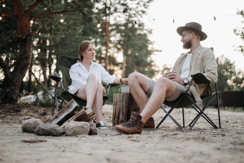 Free A couple sitting and talking at a campsite surrounded by nature, enjoying a relaxed outdoor moment. Stock Photo