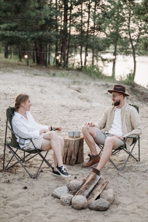 Free A couple relaxing at a campsite with coffee by a campfire in a forest setting. Stock Photo