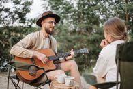 A Bearded Man Playing Guitar while Looking at the Woman Sitting in Front of Him