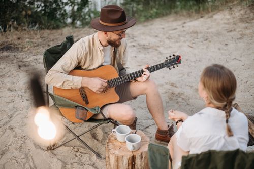 Free Two people enjoying an acoustic guitar session on a sandy beach setting with cups and chairs. Stock Photo