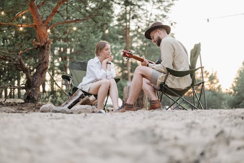 A Woman in White Long Sleeves Looking at the Man Playing Guitar