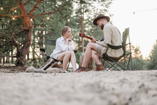 Free A couple sits by a campfire in nature, enjoying music on a summer evening. Stock Photo