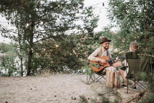 Free A man playing guitar while sitting with a woman at a scenic outdoor campsite. Stock Photo