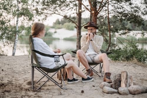 Free Relaxing outdoor scene with a couple near a campfire by the lake, playing harmonica. Stock Photo
