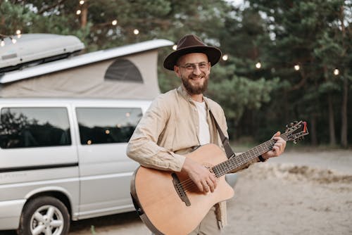 Man Holding Guitar While Standing Beside a Van