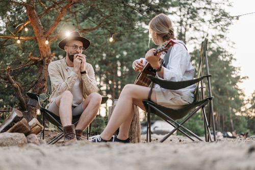 Free A harmonious moment of a couple playing guitar and harmonica while camping in a tranquil forest setting. Stock Photo