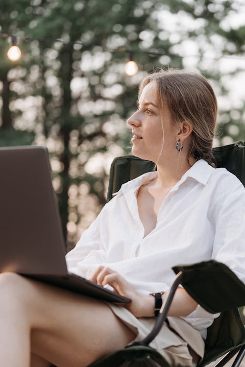 A Woman in White Long Sleeves Sitting on the Chair while Using Her Laptop