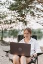 A Woman in White Long Sleeves Working on Her Laptop while Sitting on Folding Chair