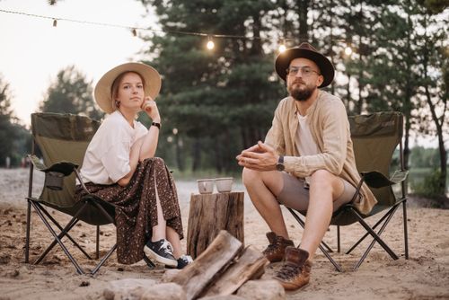 Free A couple in hats relaxes on camping chairs at sunset in a serene forest setting. Stock Photo