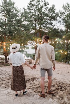 A couple holding hands in a forest setting adorned with string lights, creating a romantic atmosphere.