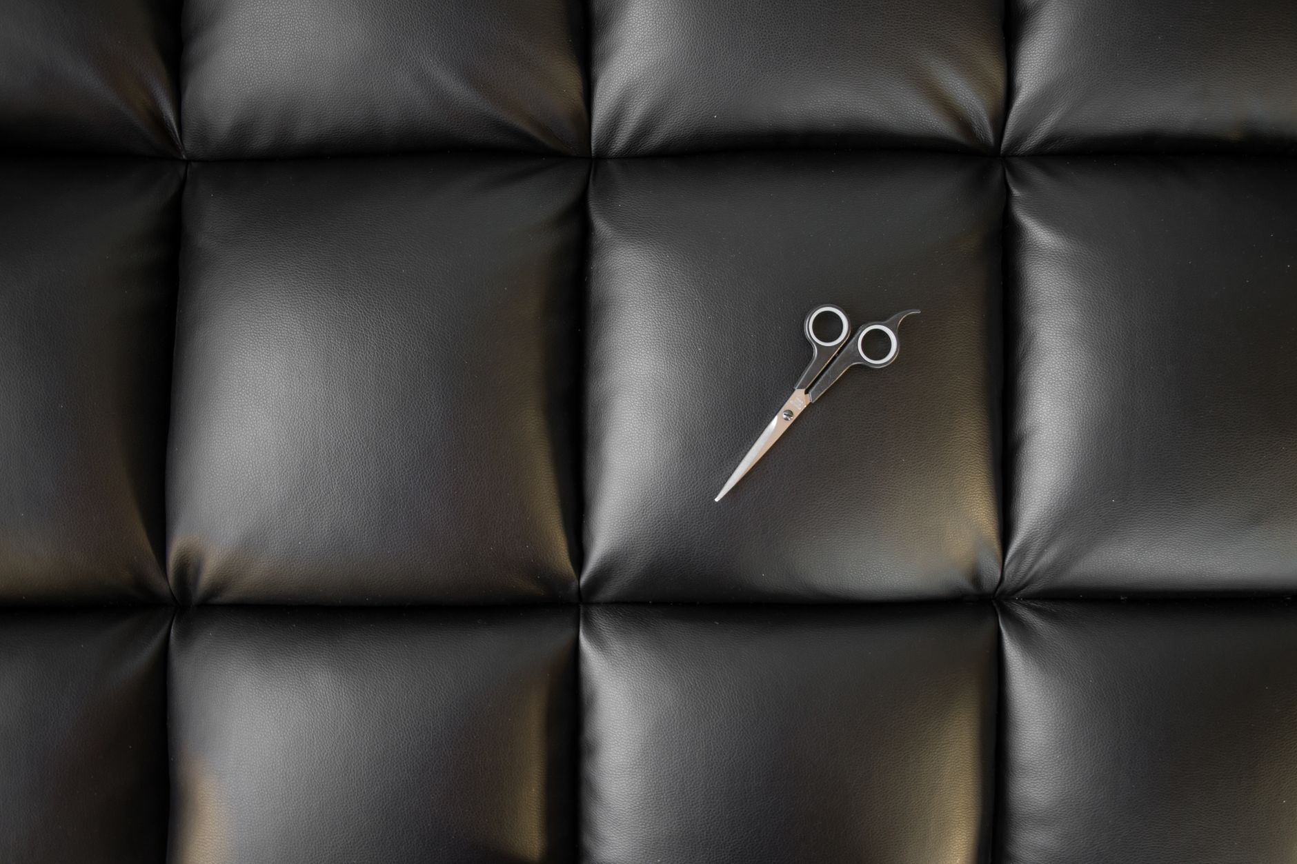 Stylish minimalist composition with scissors on a black leather quilted surface.