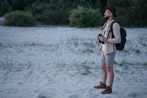 Man with a Backpack and Binoculars Standing on a Beach 