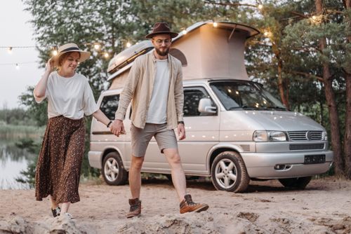 Free Couple holding hands next to camper van, embracing outdoor adventure and togetherness. Stock Photo