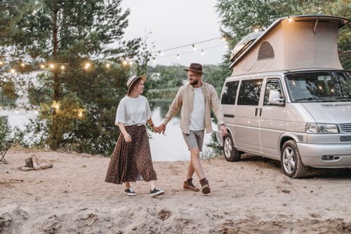 Free Happy couple walking hand-in-hand by camper van under string lights. Stock Photo