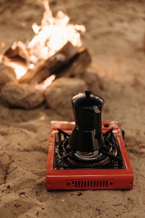 Close-up of a Coffee Pot on a Portable Stove Standing on a Beach near a Campfire 