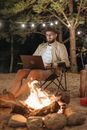 Man in White Dress Shirt Sitting on Black Folding Chair Using Macbook
