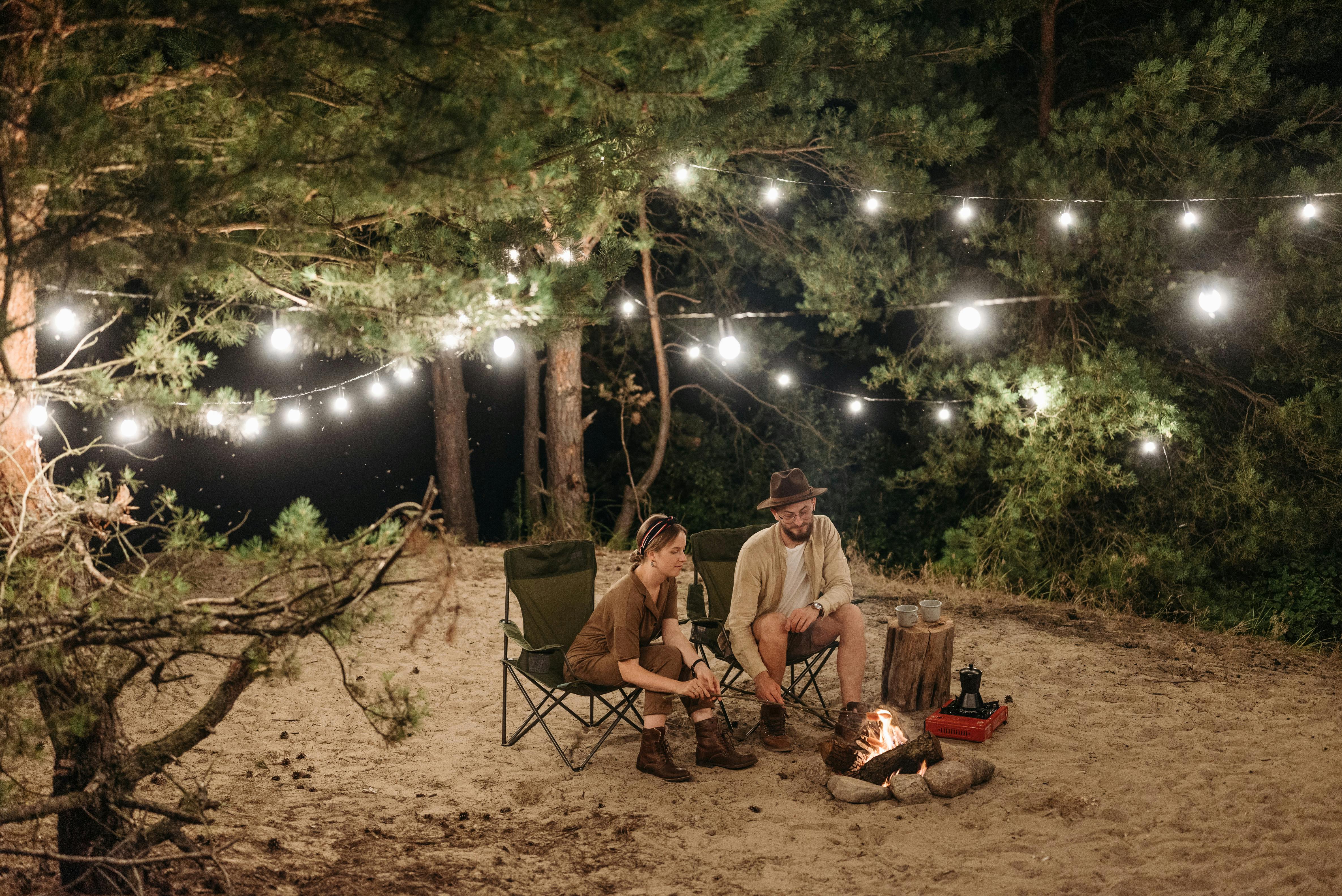 a couple sitting on chair while grilling on campfire