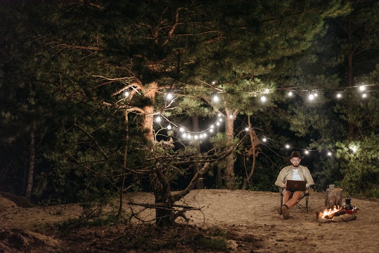 A Man Working Near The Bonfire Under The Green Trees At Night