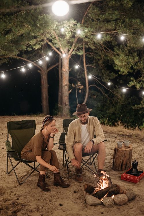Free A couple relaxes by a campfire under string lights, enjoying a serene camping night. Stock Photo
