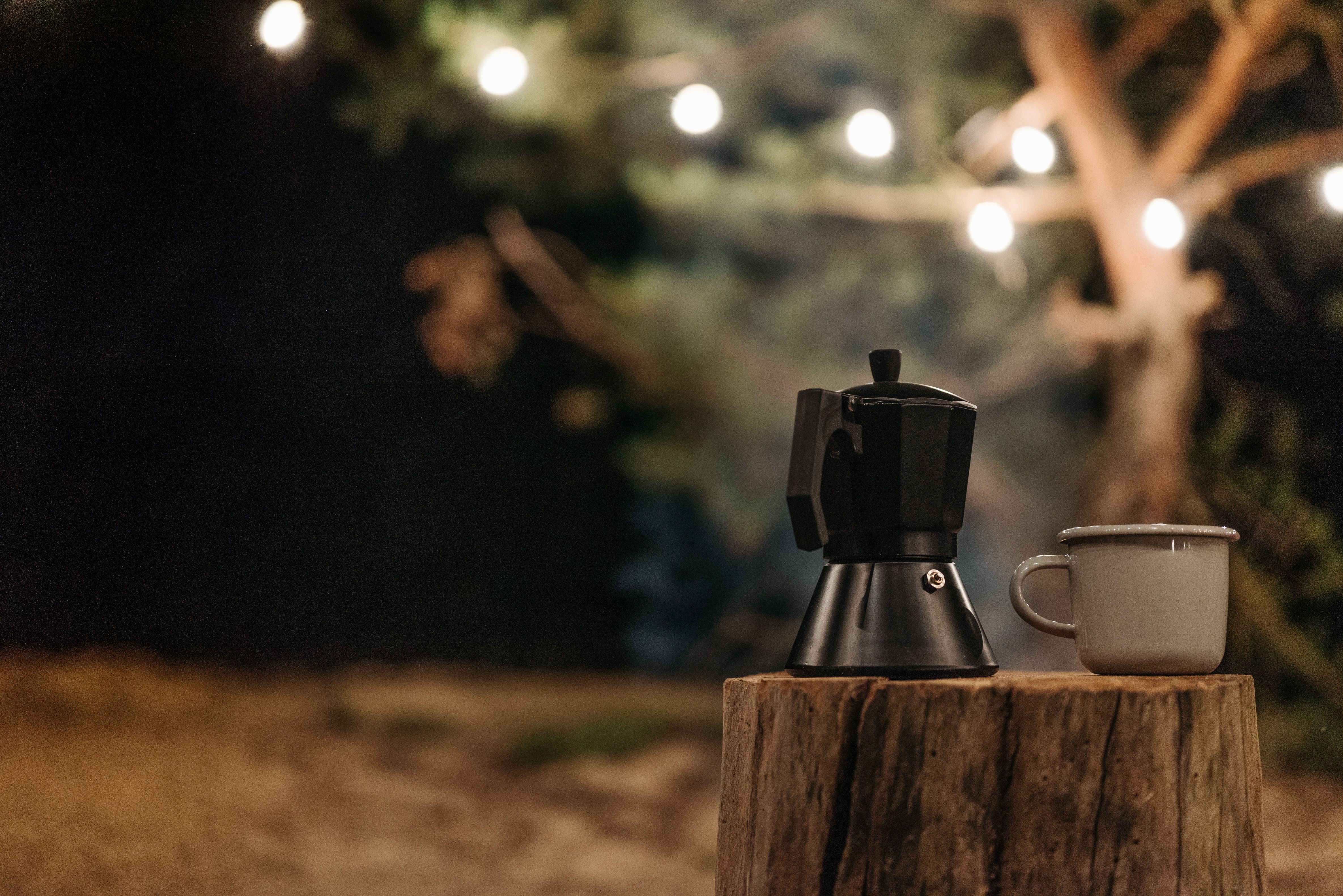 Ceramic cup and moka pot on tree stump with string lights