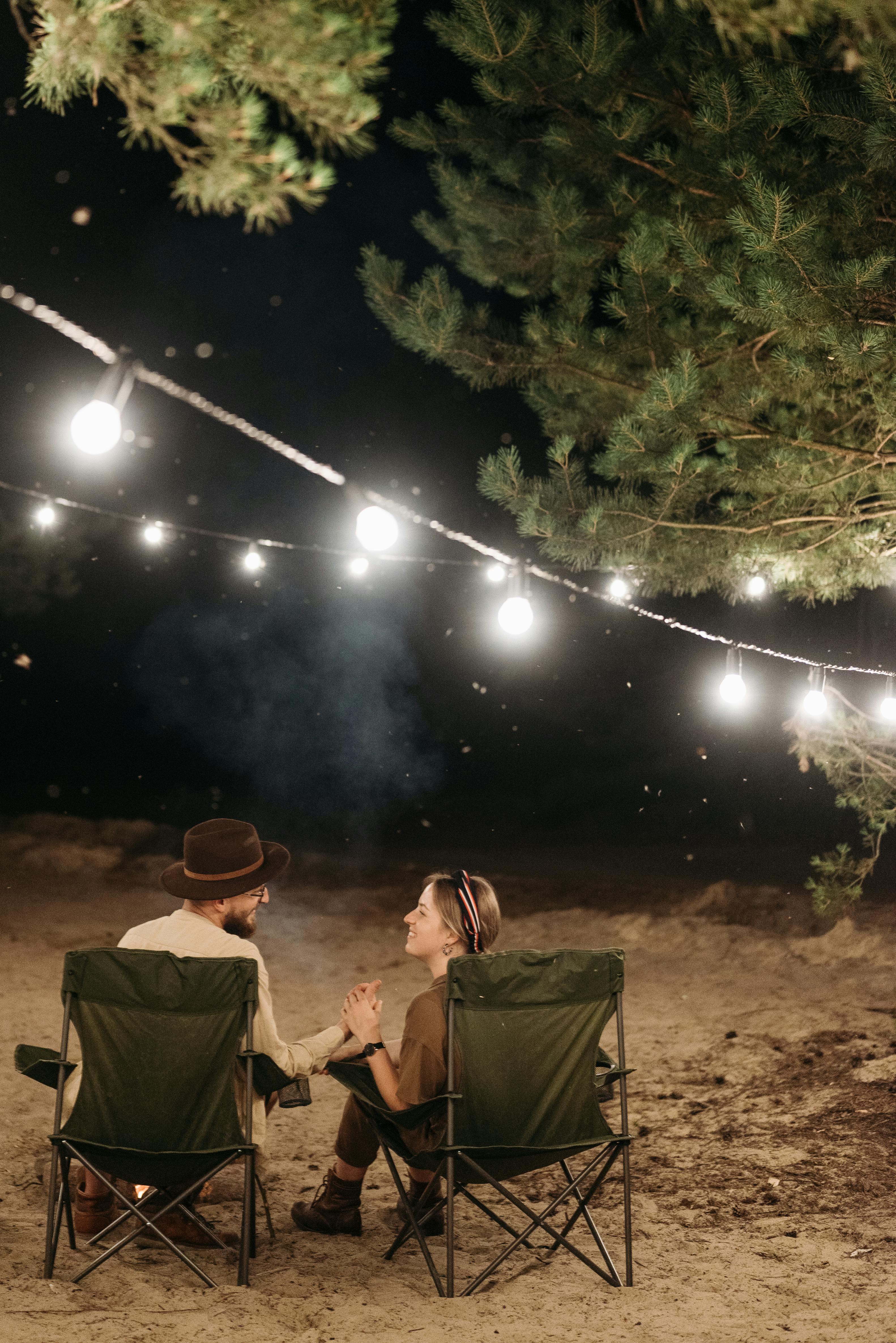 a couple holding their hands while sitting on camping chairs