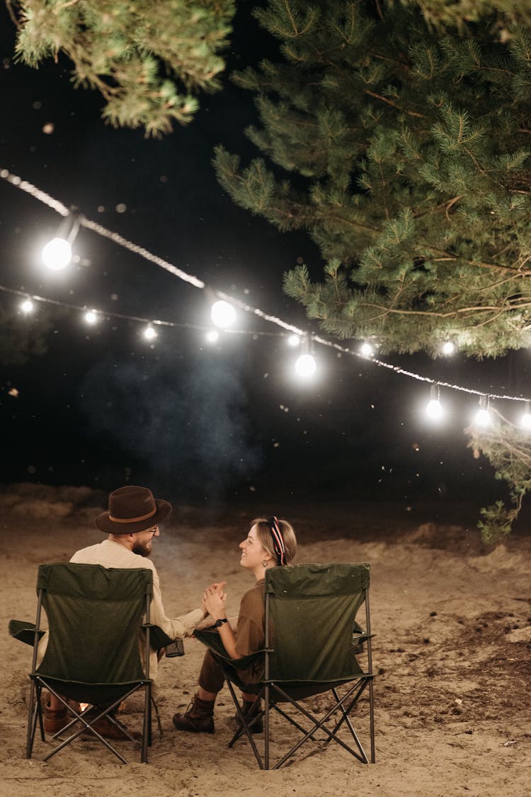 A Couple Holding Their Hands While Sitting On Camping Chairs 