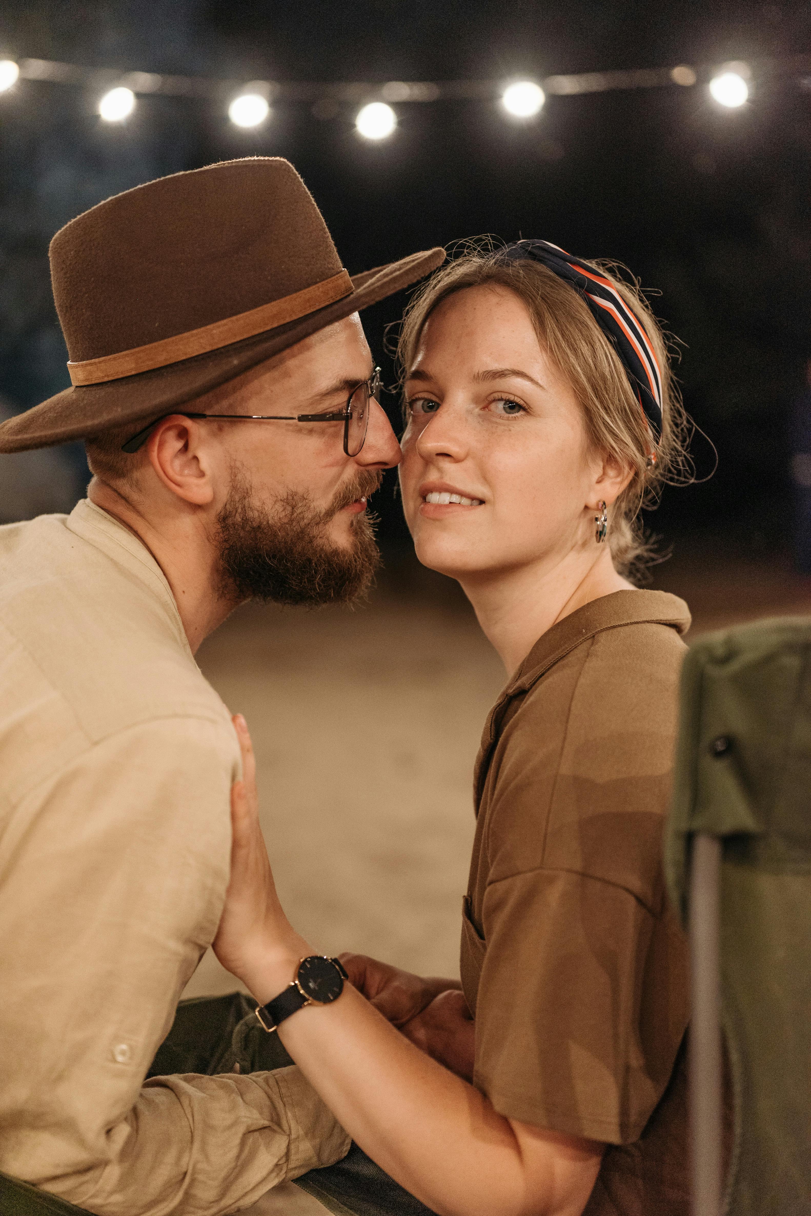 a man in brown fedora hat kissing a woman in brown shirt