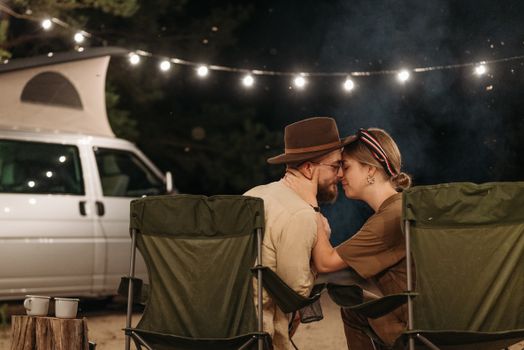 Couple enjoys a romantic moment beside van under string lights during camping trip.