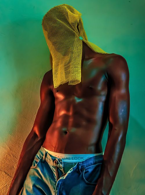 Free A muscular man posing shirtless with a yellow mesh cloth, showcasing strength and fashion. Stock Photo