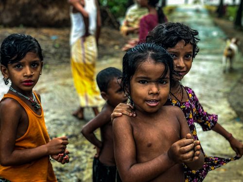 Free Joyful children enjoying a rainy day in a vibrant rural village setting. Stock Photo