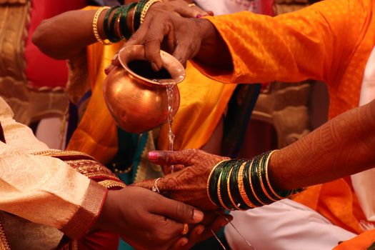 Colorful close-up of a traditional Indian wedding ceremony with water pouring ritual.