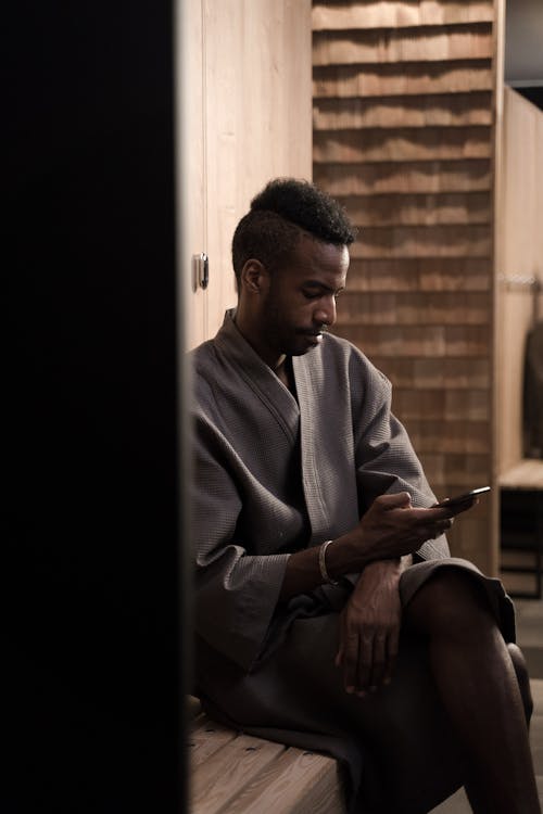 Man in a Bathrobe Sitting in a Changing Room in Spa and Using His Smartphone 