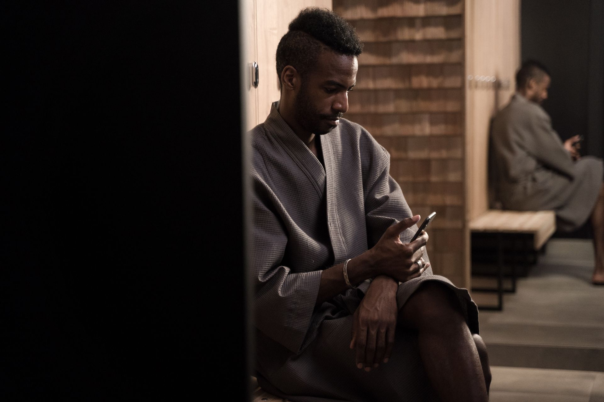 Man in a robe checking phone in a quiet modern dressing room setting.