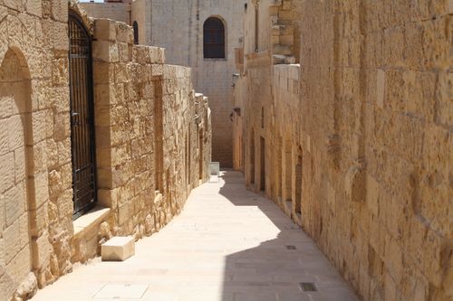 Free Explore a sunlit ancient stone alleyway lined with historic buildings, exuding timeless architectural charm. Stock Photo