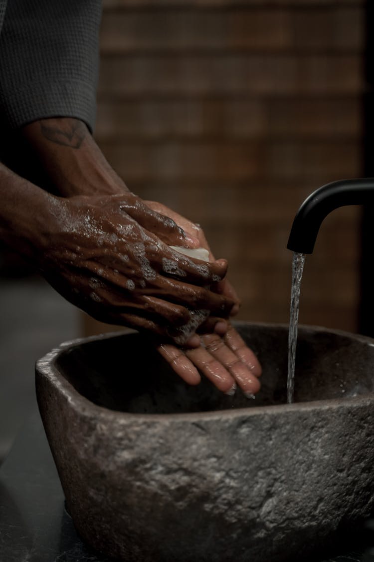 A Person Washing Hands On Sink Made Of Stone