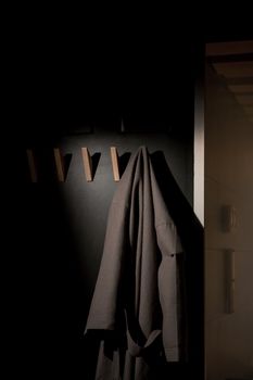 A stylish bathrobe hangs on a wooden hook in a dimly lit, modern interior setting.