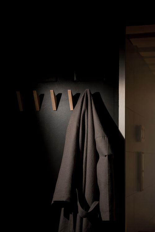Free A stylish bathrobe hangs on a wooden hook in a dimly lit, modern interior setting. Stock Photo