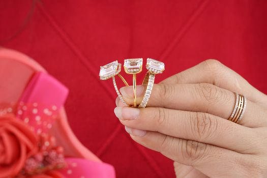 Close-up of diamond rings held in hand, showcasing luxury and elegance with a rich red background.