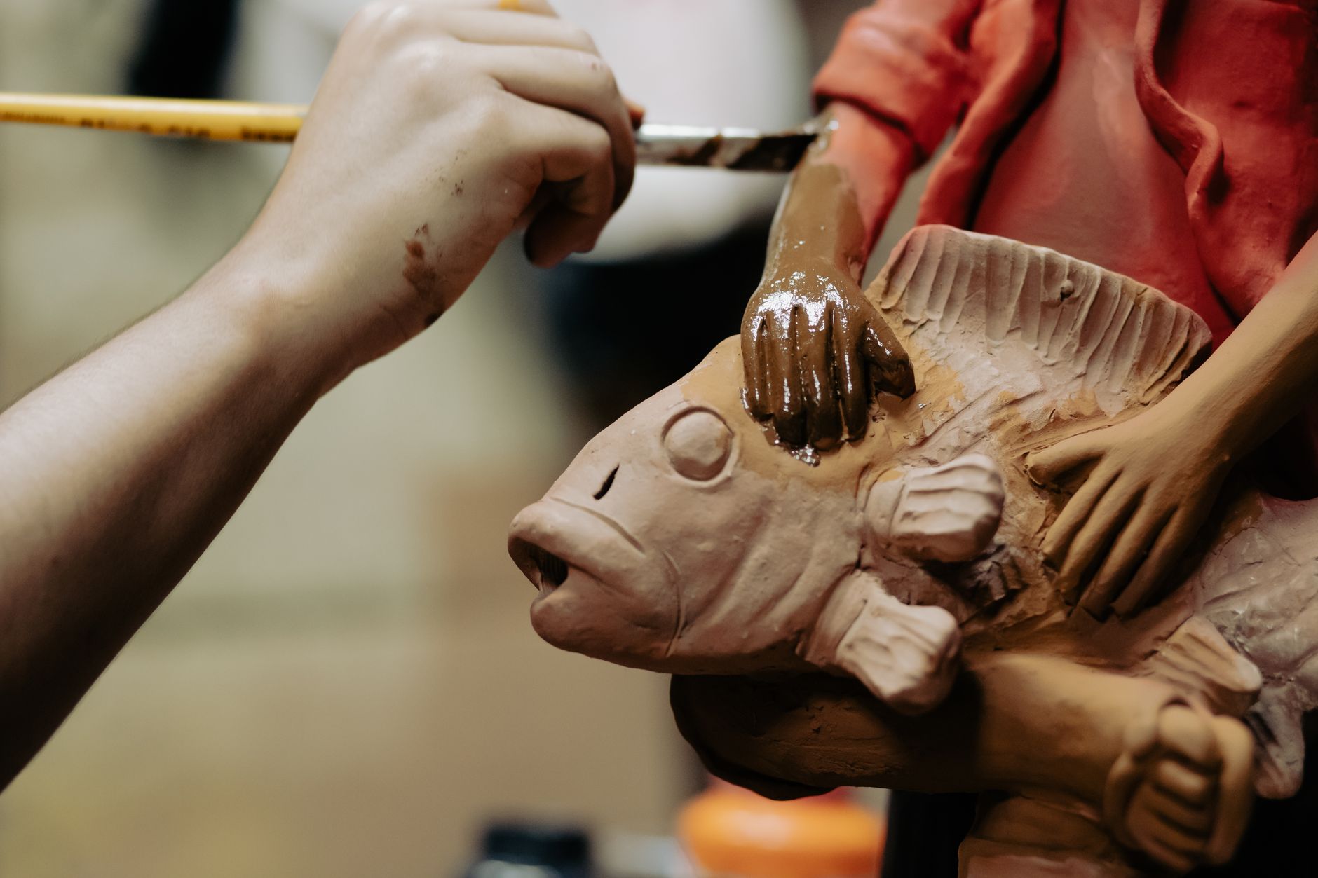 Detailed close-up of an artisan painting a clay sculpture featuring a fish design.
