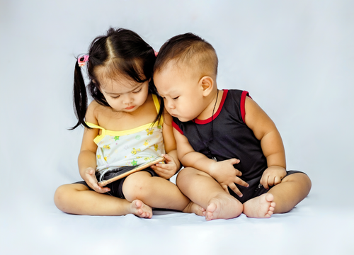 Free Two young children sitting together and exploring a tablet device in a studio setting. Stock Photo