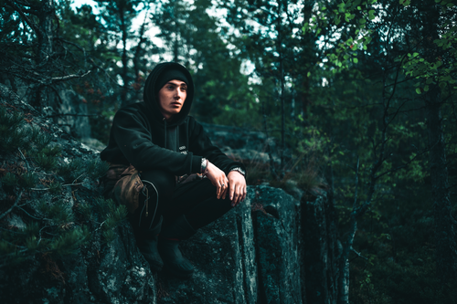 Free A young man sits on a forest edge rock, enjoying the tranquil natural surroundings. Stock Photo