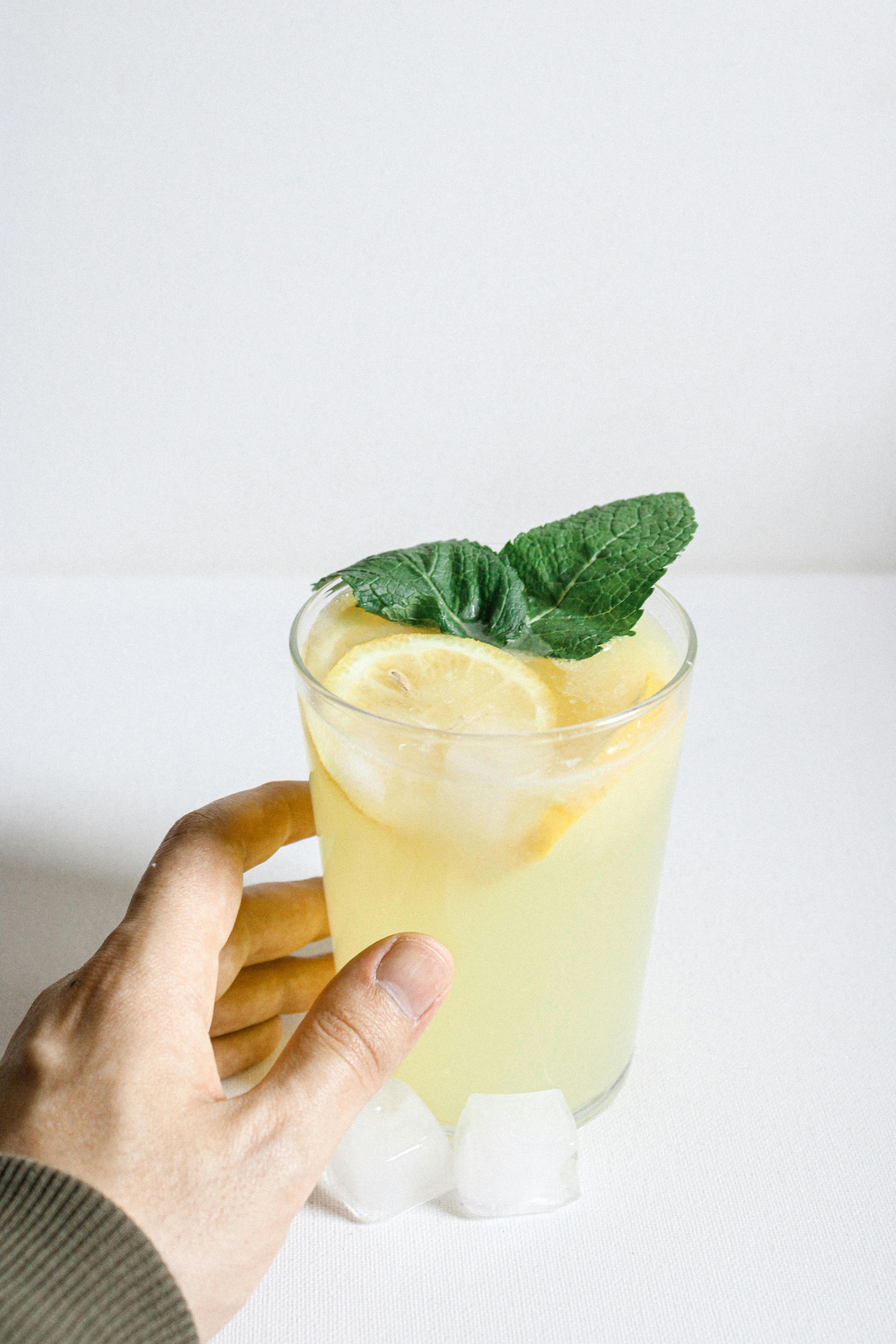 Hand holding a glass of refreshing lemonade with mint leaves on a white background.