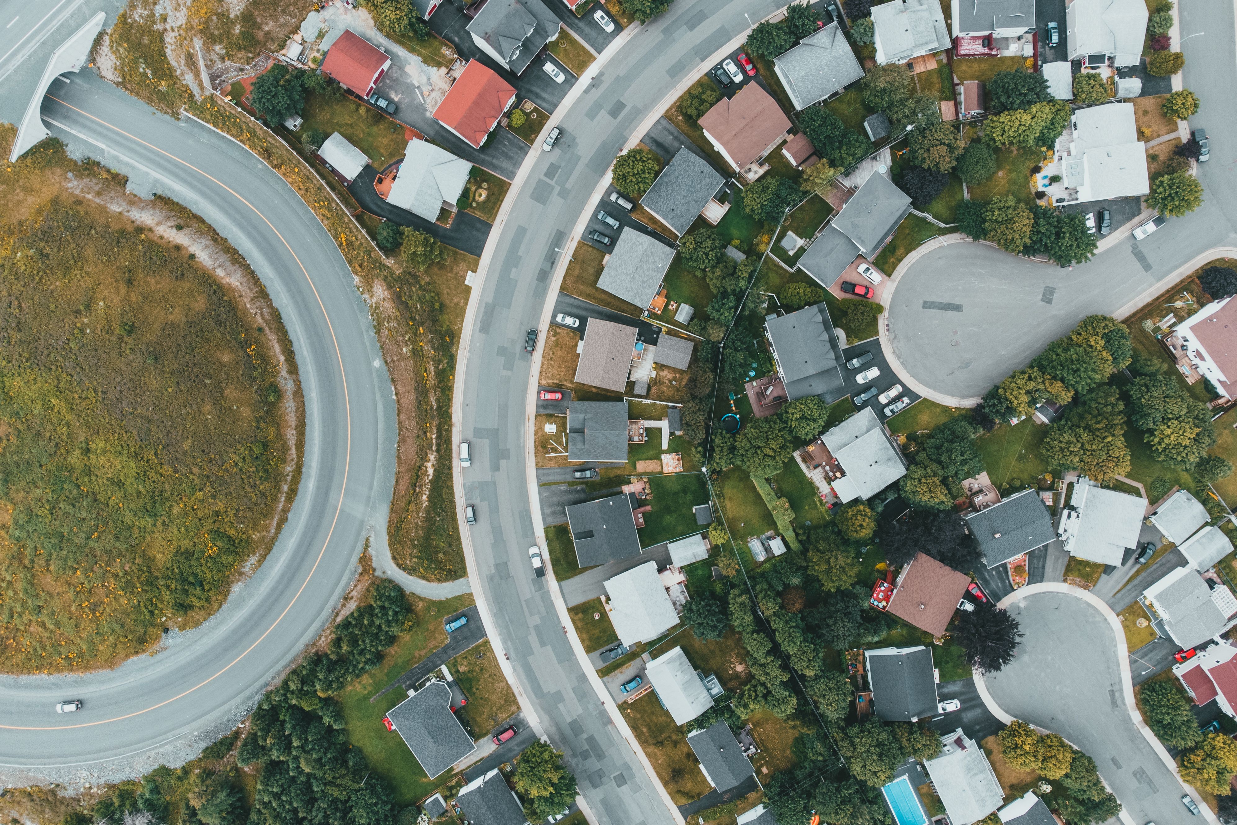 Image File Name: neighborhood-commute
Image Alt Text: Residential neighborhood with roads and vehicles traveling through the community
Image Caption: Commute and transportation costs should be included when evaluating homes for sale.