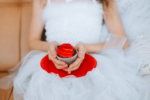 Girl in White Dress Holding Chocolate Cupcake with Red Icing